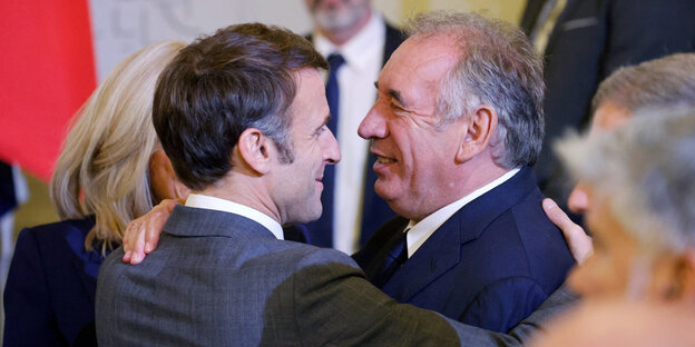 Emmanuel Macron and Francois Bayrou embrace in a friendly embrace during an event.
