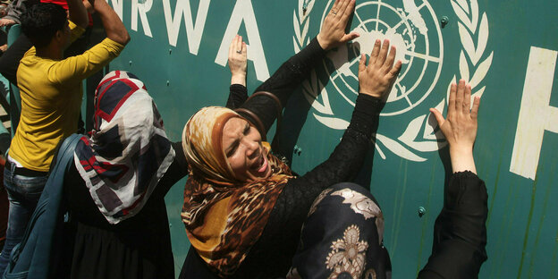 Several female protesters bang their hands against a wall with the UNRWA logo.