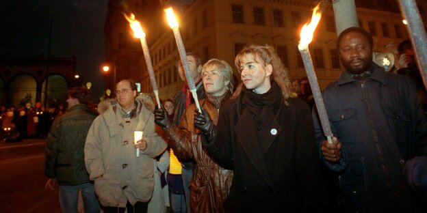 People stand on the street with burning torches and colored lights in Munich in 1992.