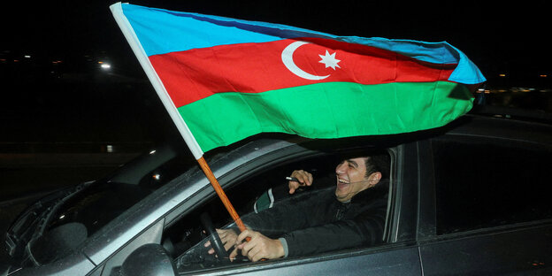A supporter of current President Ilham Aliyev laughs in the car and happily holds an Azerbaijani flag out the window.