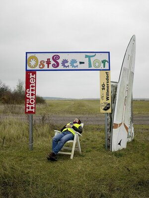 Eine Person döst auf einem Plastikstuhl unter einem improvisierten Tor mit der Aufschrift 
