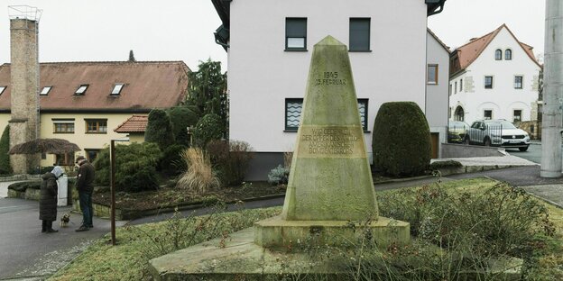 In the center of the city of Nickern, among single-family houses, there is the memorial obelisk with the inscription: We commemorate the victims of the Anglo-American terrorist bombing.  Two people with dogs are also away from home.