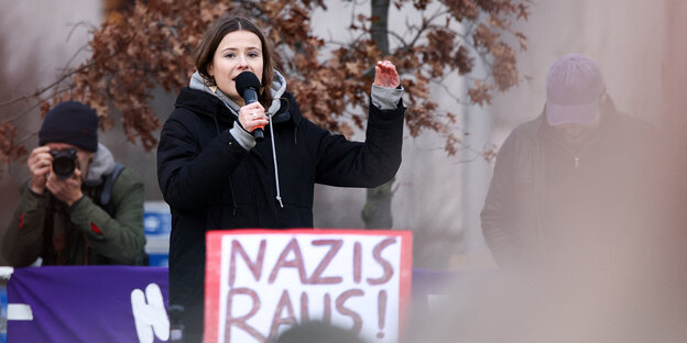 Luisa Neubauer speaks into a microphone, in front of her there is a sign 