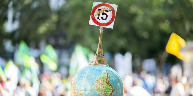 A man at the demonstration carries a globe with a miniature Eiffel Tower and the 1.5 degree goal of the Paris Climate Agreement.