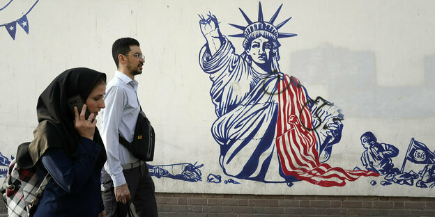 People walk past a government-organized anti-American mural on the wall of the former U.S. embassy.