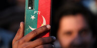Ein Mann hat ein Handy in einer rot-grünen Hülle mit der Aufschrift PTI in der Hand