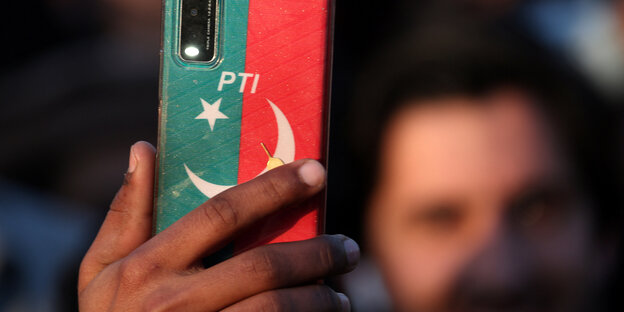 A man holds a cell phone in a red and green case with the inscription PTI in his hand
