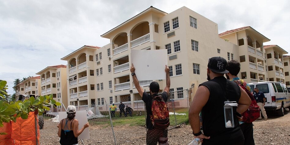 Menschen stehen vor einem Neubau und halten ein Schild in die Höhe