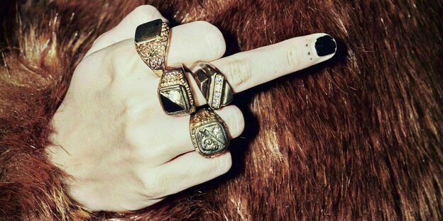 A woman is wearing a fur coat and numerous rings on her finger and gives the finger.
