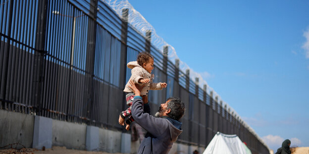People in front of a border fence with barbed wire.