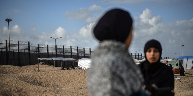 Two women in front of a border fence
