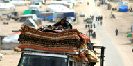 Ein Lastwagen fährt beladen mit Matrazen auf denen ein Mann liegt inder Zeltstadt von Rafah