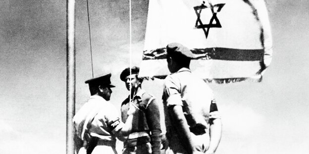 Three soldiers raise the Israeli flag.