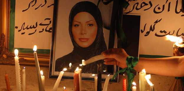 Eine Frau mit einem grünen Band um das Handgelenk macht eine Kerze bei einem Gedenkaltar an