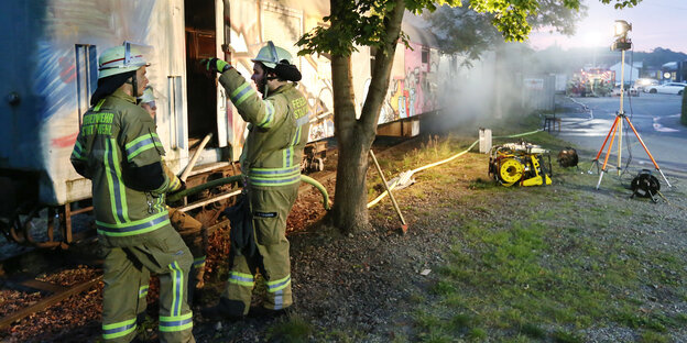 Feuerwehrleute unterhalten sich vor einem ausgebrannten Wagon Feuerwehrleute unterhalten sich vor einem ausgebrannten Wagon