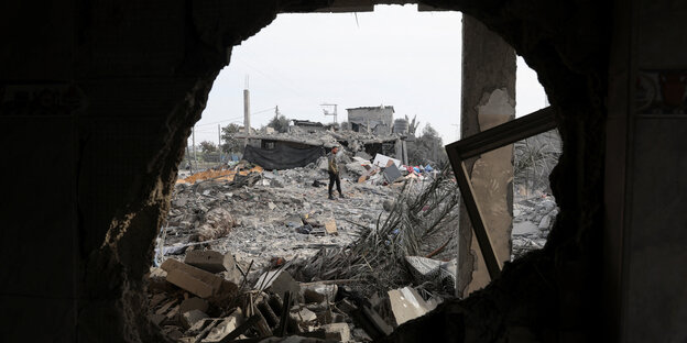 A pile of rubble with a man standing on it can be seen through a hole in the wall in Rafah, Gaza.