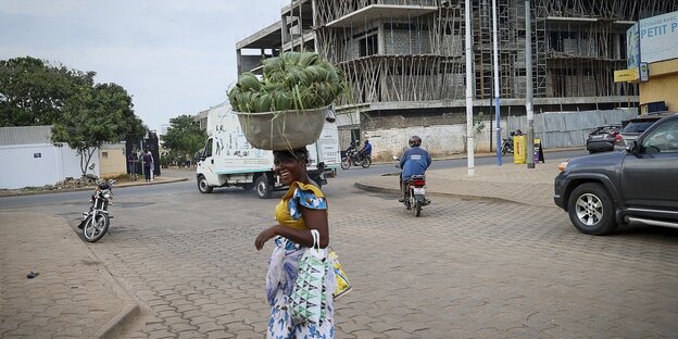 Eine Frau blickt zurück, sie trägt eine Schüssel mit lebensmitteln auf ihrem Kopf, Straßenszene