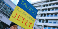 Eine Frau hält ein Blau-Gelbes Demo-Schild auf dem steht: Taurus für die Ukraine Jetzt!