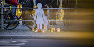 Weiße Piktogramme einer Frau und eines Kindes aus Pappe sind an einem Straßengeländer befestigt. Davor stehen brennende Windlichter auf dem Boden. Auf der Rückseite des Geländers sind Fahrräder angeschlossen.