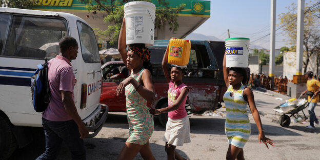 Several people carry buckets of water down a street.
