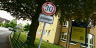 Ein Tempo-30-Schild mit Aufschrift "Altenheim" am Straßenrand vor gelben Haus