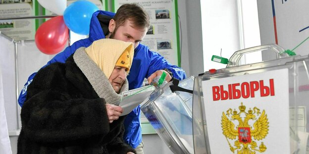Eine ältere Frau stimmt im Wahllokal ab, sie wird von einem Wahlhelfer unterstützt