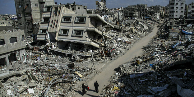 Taken from an elevated position on a street between completely destroyed buildings in a Gaza city.  People walk through it.