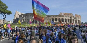 Viele Menschen laufen in Rom eine Straße entlang und schwenken eine Regenbogenflagge
