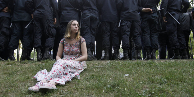 A woman sitting on the grass in front of a police line at an LGBT demonstration