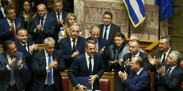 Greek Prime Minister Kyriakos Mitsotakis (M) is applauded by his party's deputies during a parliamentary session