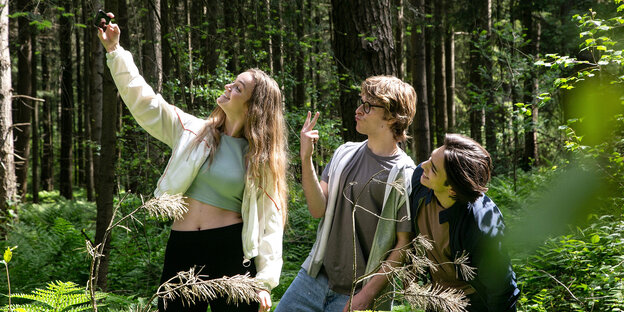 Three teenagers in the forest, the girl takes a selfie with the two young people