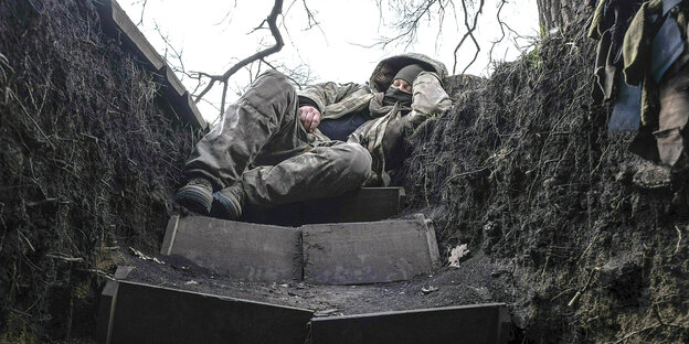A soldier sleeps in a trench.