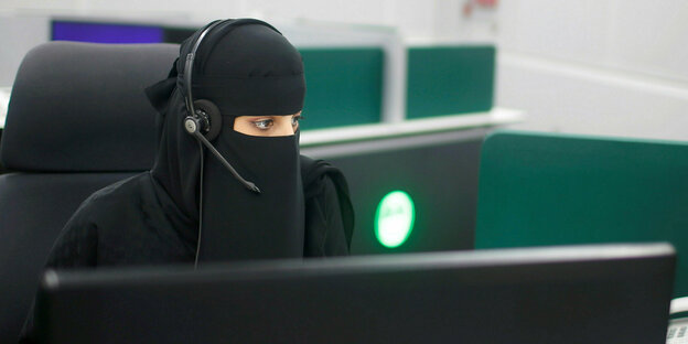Eine voll verschleierte Frau mit Headset zwischen Computern