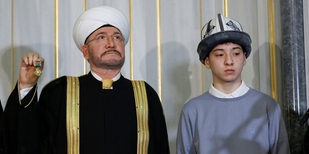 Islam Khalilov is dressed in traditional clothing at a ceremony alongside a member of the Council of Muftis.