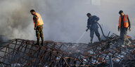 3 Männer stehen auf einem ausgebrannten Eisengerüst und löschen