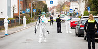 Ermittler in weißen Anzügen stehen am Tatort auf einer Straße