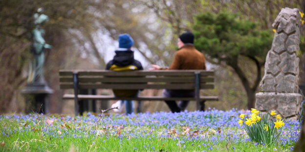 Sibirischer Blaustern (Scilla siberica) und Narzissen blühen, während Passanten auf einer Parkbank sitzen
