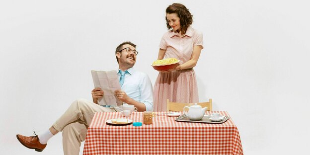 A woman serves apple pie to her husband while he reads the newspaper.