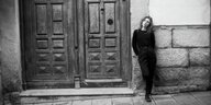 Julia Holter lehnt mit dem Rücken an einer Hauswand neben einer mächtigen Tür