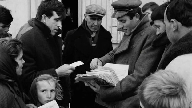 Schwarz-weiß-Foto, das einen Mann zeigt, der Zettel an Menschen um ihn herum verteilt