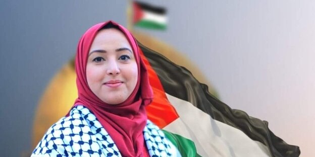 Eine Frau steht vor einer Palästina Flagge.