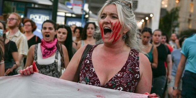 Aus Protest haben sich Frauen mit ihren Händen rote Farbe ins Gesicht gedruckt.