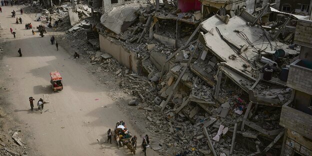 People move through a destroyed city.  Photographed from above diagonally so that people are small next to the ruins.
