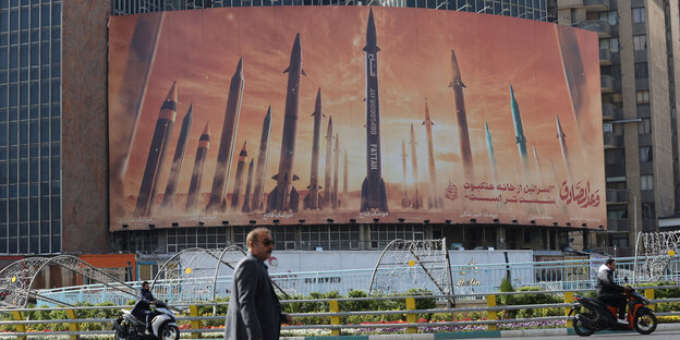 Rockets lined up on an advertising billboard in Tehran.  A man passes by.