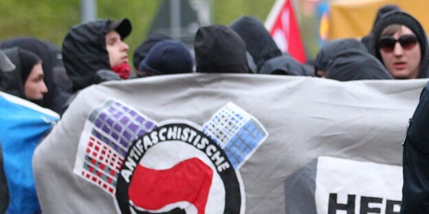 Vermummte Menschen stehen hinter einem Plakat. Vermummte Menschen stehen hinter einem Plakat.