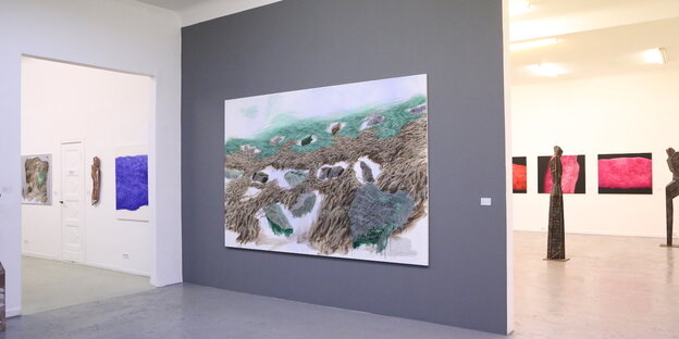 Blick in die Ausstellungsräume der Galerie Tammen. Im Zentrum der Aufnahme ist eine graue Wand zu sehen, auf der Harald Gnades Gemälde "Implant" hängt. Es zeigt eine abstrahierte Landschaftsszene mit grünen Elementen, die Grasboden andeuten. Im Vordergrun