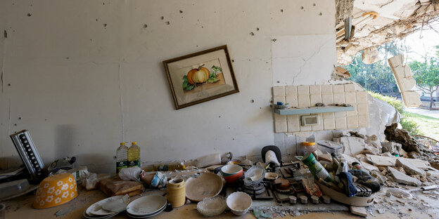 A wall with bullet holes, dishes on the sink shelf, a painting hanging crooked