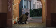 Eine obdachlose Person richtet sich in einem Durchgang ihr Nachtlager ein.
