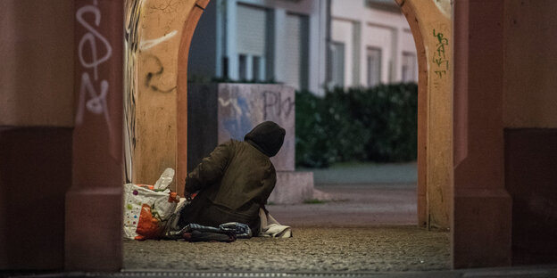 Eine obdachlose Person richtet sich in einem Durchgang ihr Nachtlager ein.