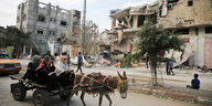 Palästinenser*innen auf einem Wagen mit einem Esel inmitten zerbombter und eingestürzter Häuser